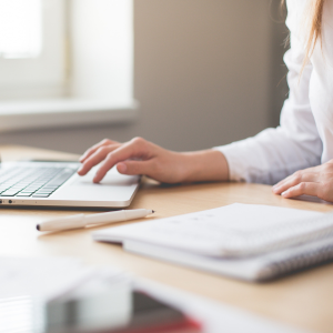 Person typing on a laptop with a notebook on the desk.
