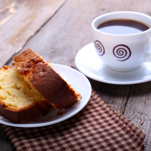 A slice of cake next to a cup of coffee.
