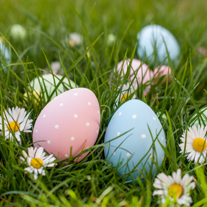 Two decorated eggs on the grass with some daisies growing.