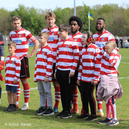 Kingstonian players standing on the football pitch with young carers all wearing the Kingstonian red and white striped kit.