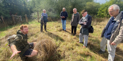 Group of men listening to talk in a field ready for scything