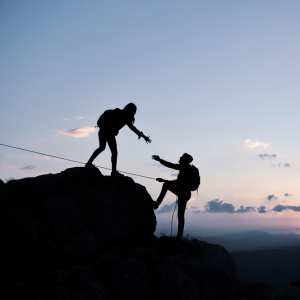 Two people on a mountain - one helping the other up.