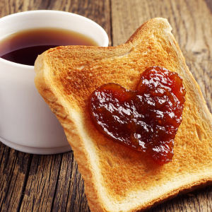 A nice cup of tea with a slice of jam propped up against it. The jam is in a heart shape.